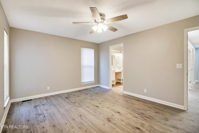 interior space with a textured ceiling, light hardwood / wood-style floors, ceiling fan, and ensuite bathroom