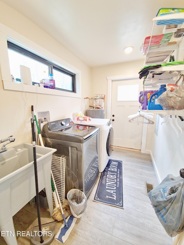 clothes washing area with sink, light hardwood / wood-style flooring, and washing machine and clothes dryer