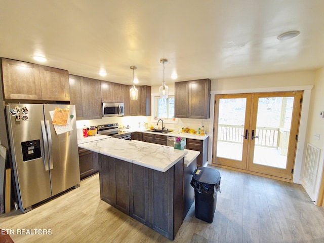 kitchen featuring a kitchen island, appliances with stainless steel finishes, decorative light fixtures, sink, and light wood-type flooring