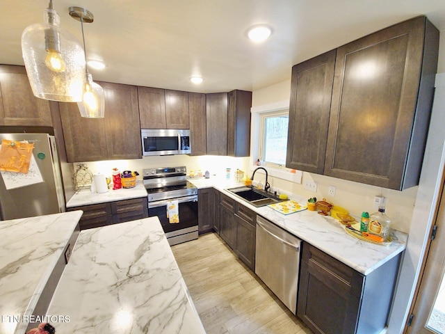 kitchen with sink, light stone counters, dark brown cabinets, pendant lighting, and stainless steel appliances