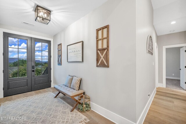 foyer entrance with a notable chandelier, light wood-type flooring, and french doors