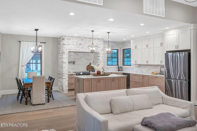 kitchen featuring stainless steel fridge, a kitchen island, light hardwood / wood-style flooring, decorative light fixtures, and white cabinetry