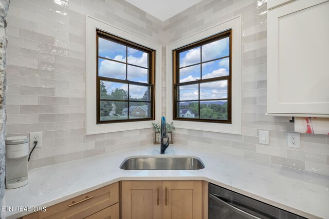 kitchen featuring light stone countertops, white cabinets, stainless steel dishwasher, and sink