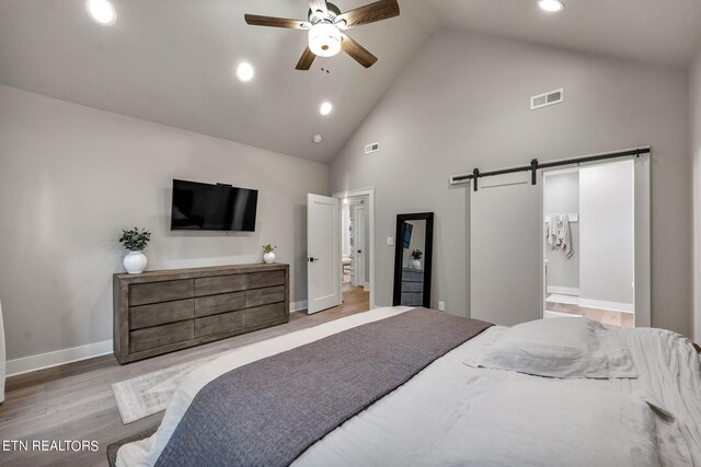 bedroom featuring light wood-type flooring, a barn door, high vaulted ceiling, connected bathroom, and ceiling fan