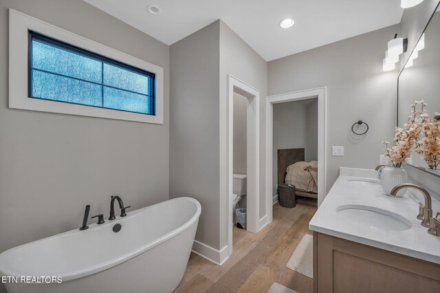 bathroom featuring vanity, a tub to relax in, hardwood / wood-style floors, and toilet