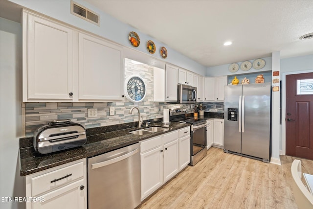 kitchen with white cabinets, light hardwood / wood-style flooring, stainless steel appliances, dark stone countertops, and decorative backsplash