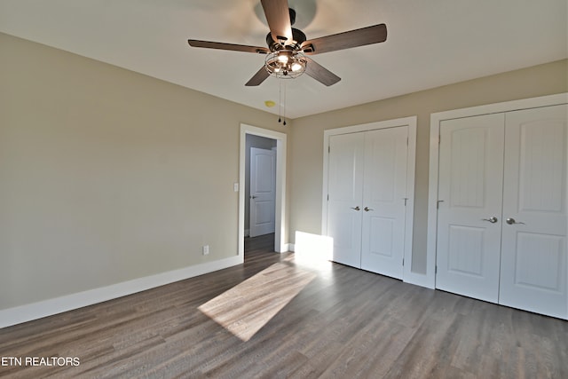 unfurnished bedroom featuring ceiling fan, multiple closets, and dark hardwood / wood-style floors