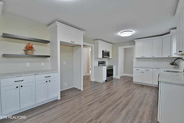 kitchen with sink, white cabinets, light hardwood / wood-style flooring, appliances with stainless steel finishes, and light stone countertops