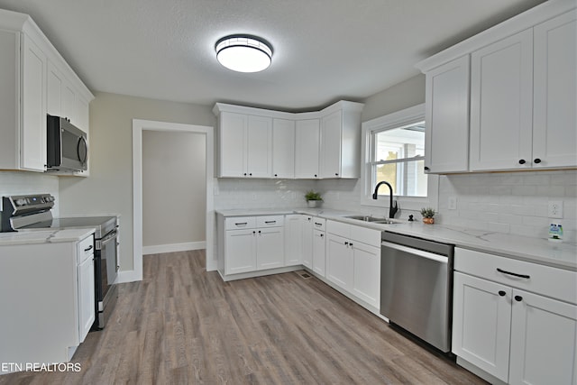 kitchen featuring light hardwood / wood-style floors, tasteful backsplash, sink, white cabinets, and appliances with stainless steel finishes