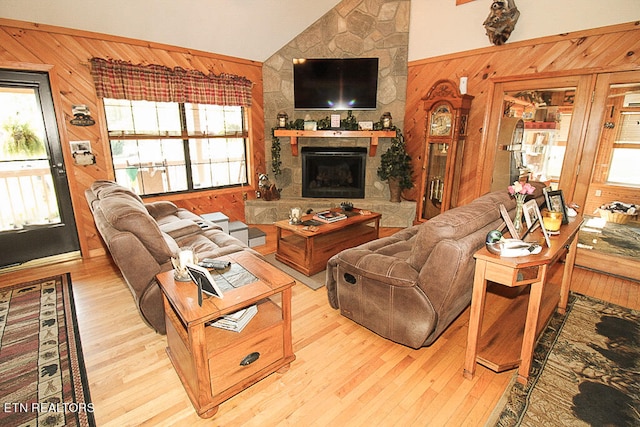 living room with a stone fireplace, light wood-type flooring, vaulted ceiling, and a wealth of natural light