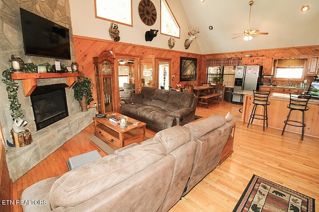 living room featuring light hardwood / wood-style floors, a fireplace, high vaulted ceiling, wooden walls, and ceiling fan