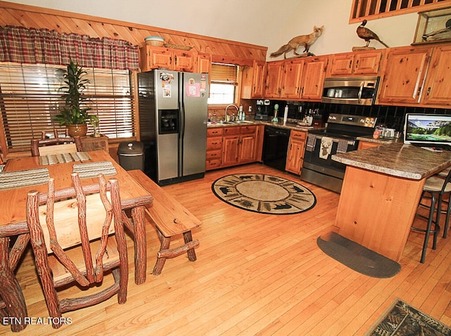 kitchen featuring sink, light hardwood / wood-style flooring, backsplash, appliances with stainless steel finishes, and a breakfast bar