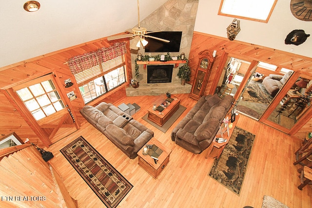 living room with a fireplace, wooden walls, ceiling fan, and high vaulted ceiling