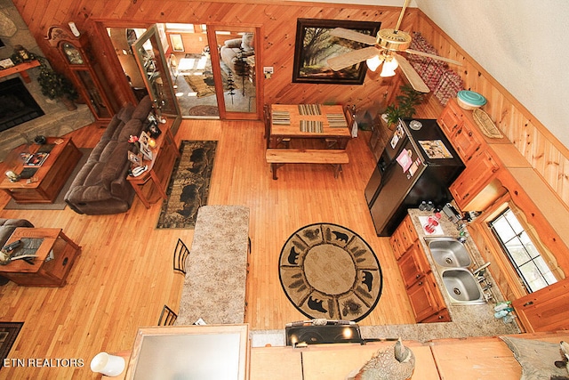 living room with ceiling fan, wood walls, wood-type flooring, and a towering ceiling