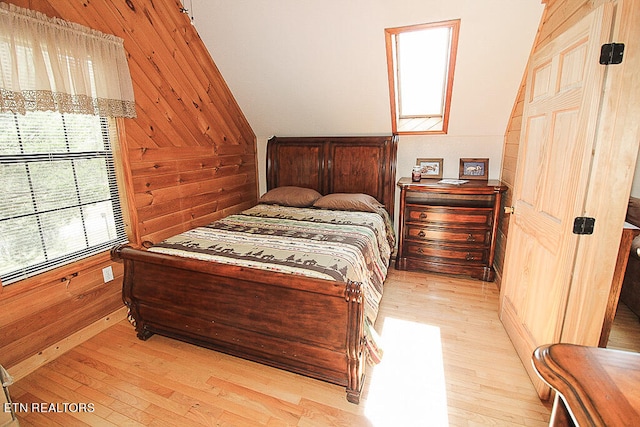 bedroom featuring light hardwood / wood-style flooring, wooden walls, and lofted ceiling