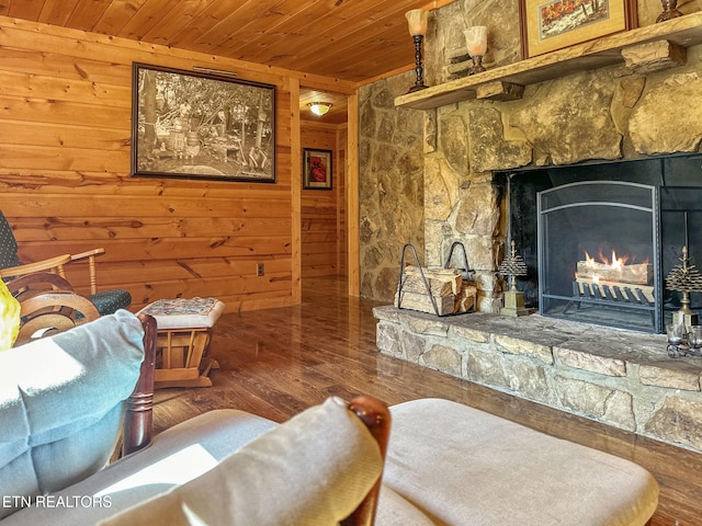 sitting room with wood-type flooring, a stone fireplace, wooden ceiling, and wood walls