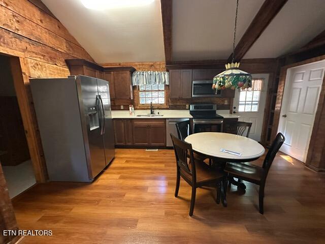 kitchen with light hardwood / wood-style floors, appliances with stainless steel finishes, a wealth of natural light, and vaulted ceiling with beams