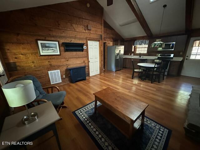 living room with wood walls, hardwood / wood-style flooring, sink, lofted ceiling with beams, and ceiling fan