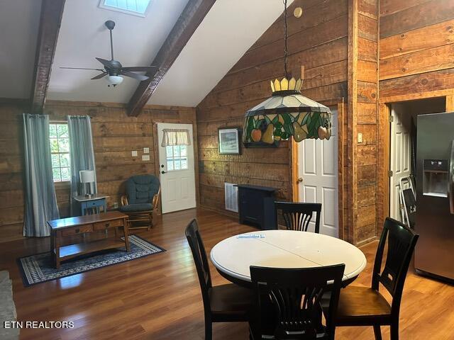 dining room featuring wooden walls, vaulted ceiling with skylight, hardwood / wood-style flooring, and ceiling fan