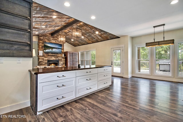 bar featuring hanging light fixtures, lofted ceiling with beams, dark wood-type flooring, white cabinets, and a fireplace