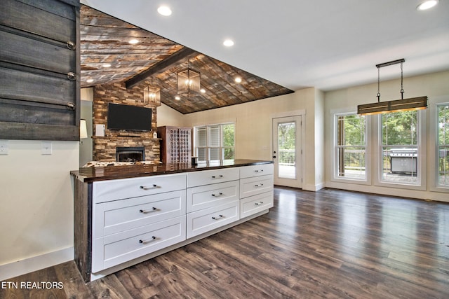 kitchen featuring lofted ceiling with beams, dark hardwood / wood-style floors, white cabinetry, hanging light fixtures, and a stone fireplace