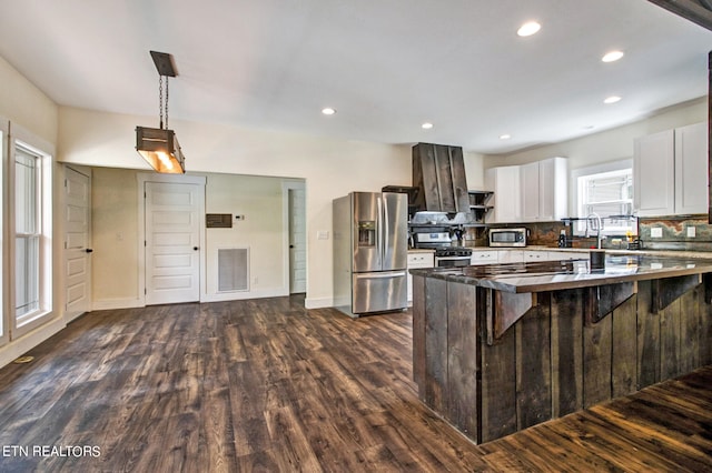 kitchen with white cabinets, appliances with stainless steel finishes, dark hardwood / wood-style floors, and a breakfast bar