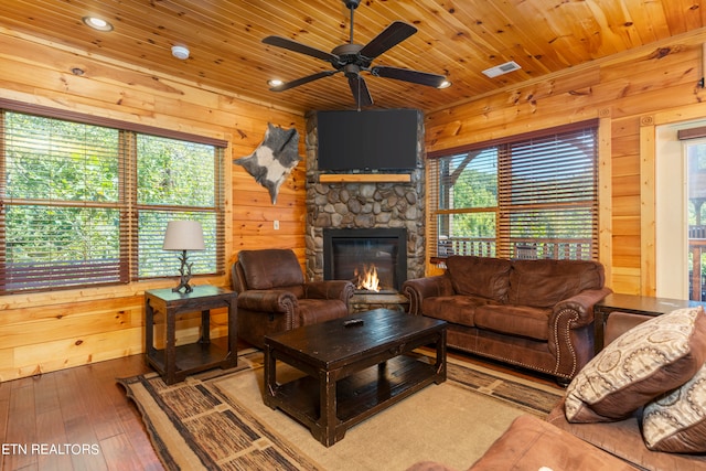 living room with a stone fireplace, wood ceiling, wooden walls, hardwood / wood-style flooring, and ceiling fan