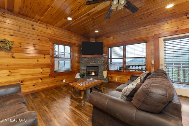 living room featuring wood walls, wooden ceiling, a stone fireplace, ceiling fan, and wood-type flooring