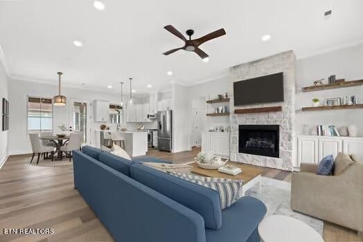 living room featuring ceiling fan, a stone fireplace, ornamental molding, and light hardwood / wood-style flooring