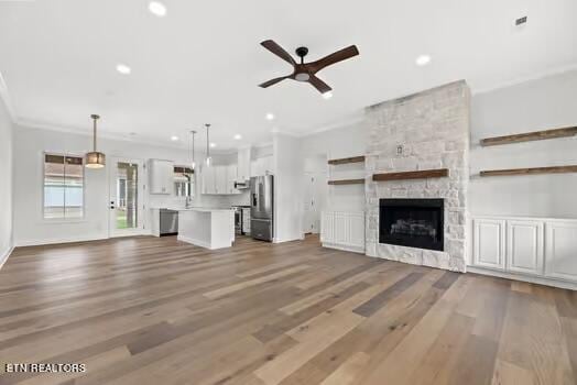 unfurnished living room featuring a fireplace, hardwood / wood-style floors, ceiling fan, and ornamental molding