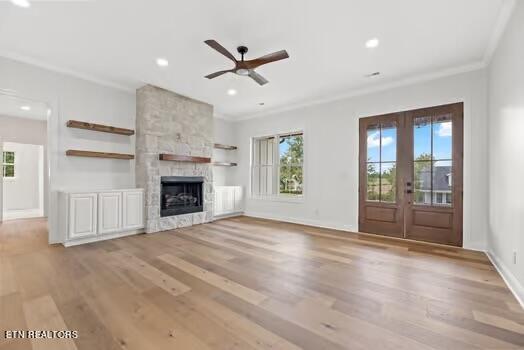 unfurnished living room with a fireplace, french doors, ceiling fan, and crown molding