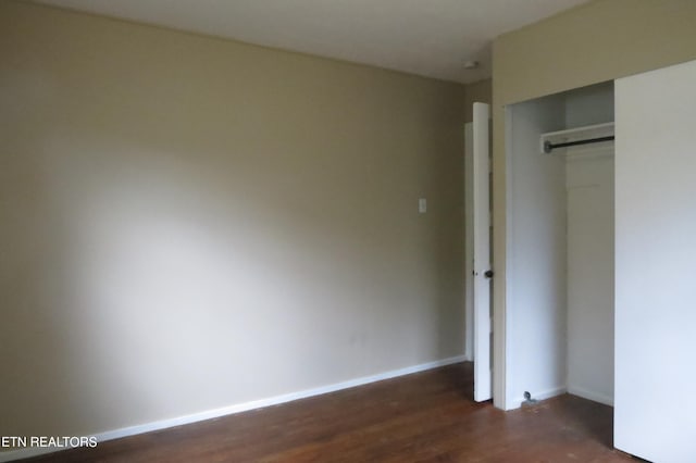 unfurnished bedroom featuring a closet, dark wood-type flooring, and a barn door