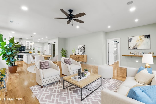 living room with ceiling fan, a barn door, and light hardwood / wood-style flooring