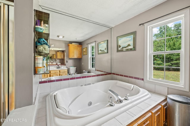 bathroom featuring tiled tub, a textured ceiling, vanity, and toilet