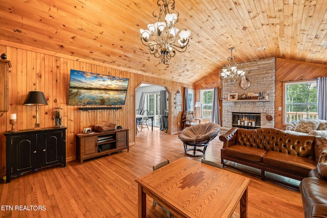 living room with wooden ceiling, a stone fireplace, wooden walls, and an inviting chandelier