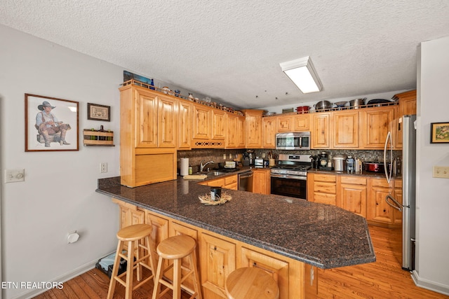 kitchen featuring appliances with stainless steel finishes, light hardwood / wood-style floors, backsplash, kitchen peninsula, and a breakfast bar area