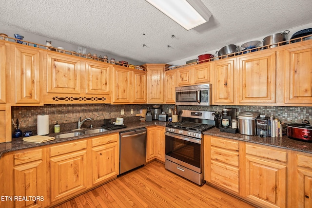 kitchen with light wood-type flooring, dark stone countertops, a textured ceiling, and appliances with stainless steel finishes