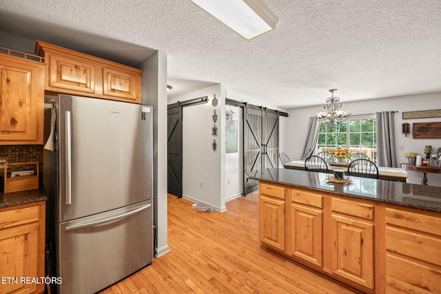 kitchen featuring a textured ceiling, a notable chandelier, a barn door, light hardwood / wood-style flooring, and stainless steel refrigerator