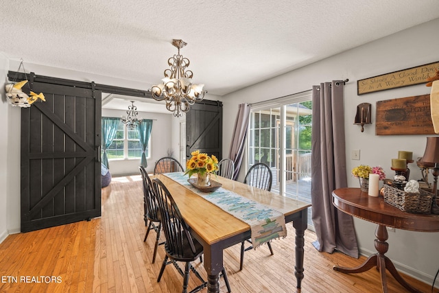 dining room with a barn door, a textured ceiling, an inviting chandelier, and light hardwood / wood-style flooring