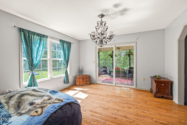 bedroom featuring light hardwood / wood-style flooring, a chandelier, a textured ceiling, and access to outside