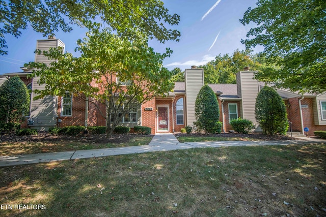 view of front of property with a front yard, brick siding, and a chimney