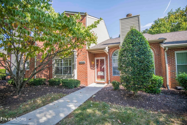 property entrance with a shingled roof, a chimney, and brick siding