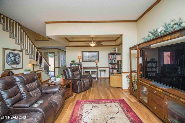 living room with ceiling fan, ornamental molding, a tray ceiling, and light hardwood / wood-style floors