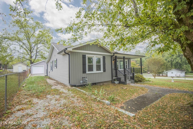 view of front of property featuring fence, driveway, an outbuilding, a detached garage, and a porch