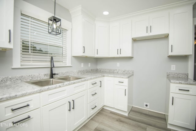 kitchen with light wood finished floors, white cabinets, a sink, baseboards, and hanging light fixtures