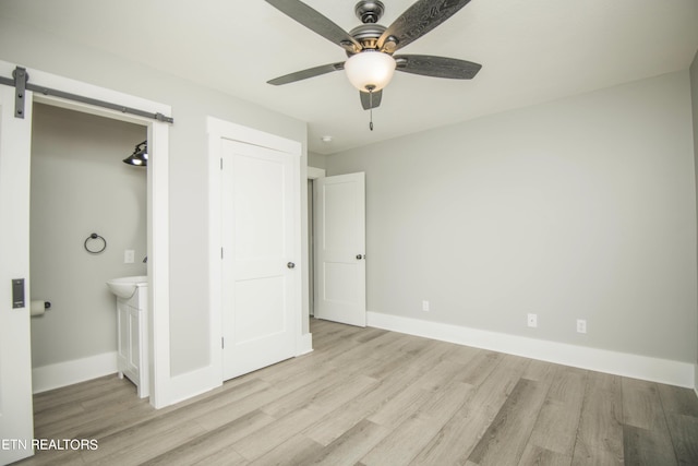 unfurnished bedroom with ensuite bath, a barn door, baseboards, and wood finished floors