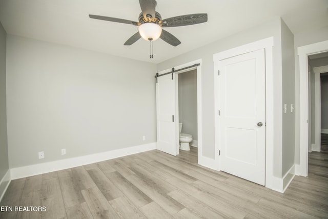 unfurnished bedroom with a barn door, baseboards, wood finished floors, ceiling fan, and ensuite bath