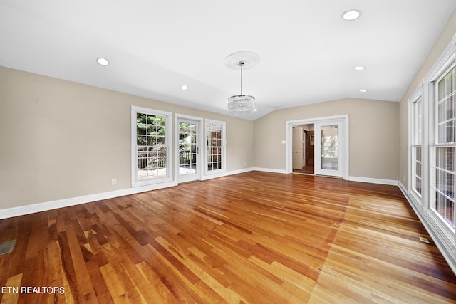 unfurnished living room featuring a notable chandelier, vaulted ceiling, and light hardwood / wood-style flooring