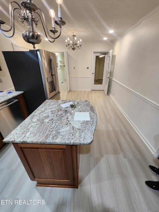 kitchen with appliances with stainless steel finishes, light wood-type flooring, light stone counters, and a notable chandelier