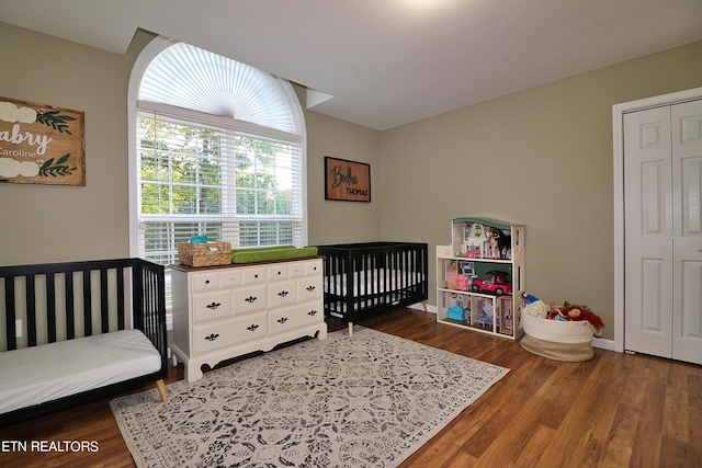 bedroom with a crib, a closet, and dark hardwood / wood-style flooring